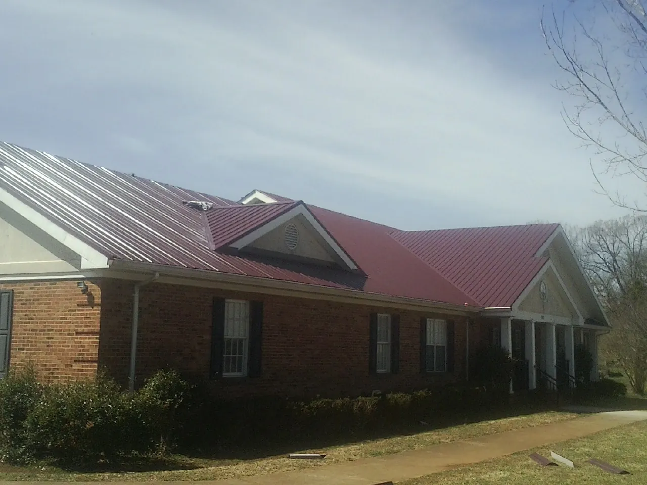 Red metal roof with gabled entries on a long brick building, from a Hail Damage Roof Repair job in Calhoun