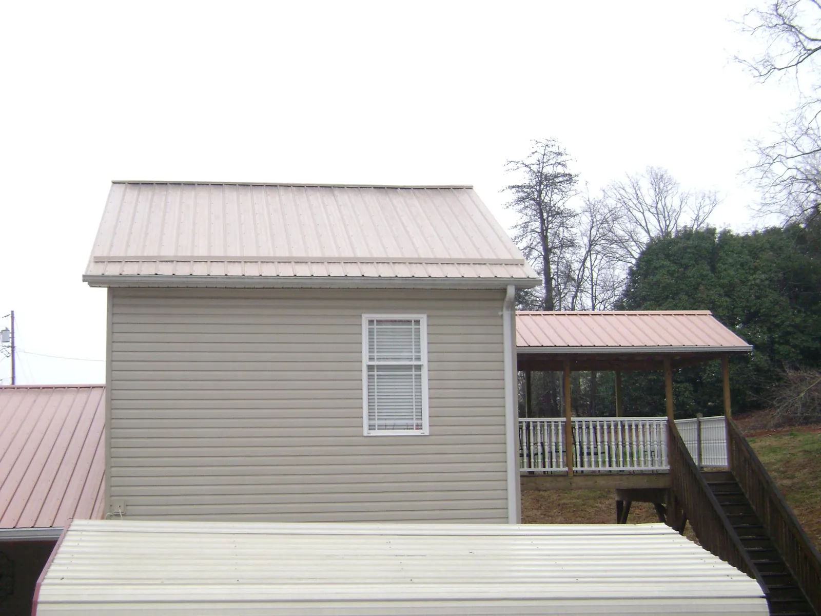 Tan metal roofs on a two story addition and attached porch, from a Roof Replacement job in Calhoun
